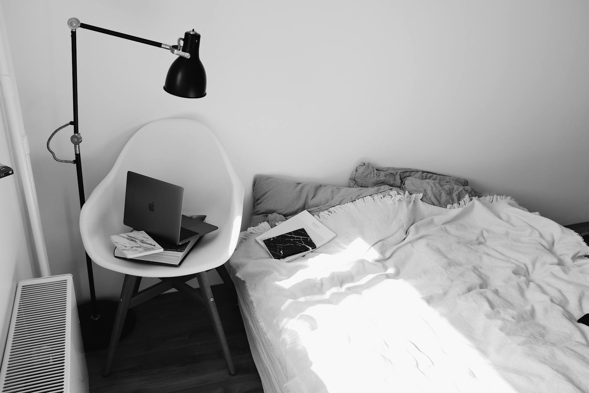 Laptop na krześle w jasnej, monochromatycznej sypialni z łóżkiem