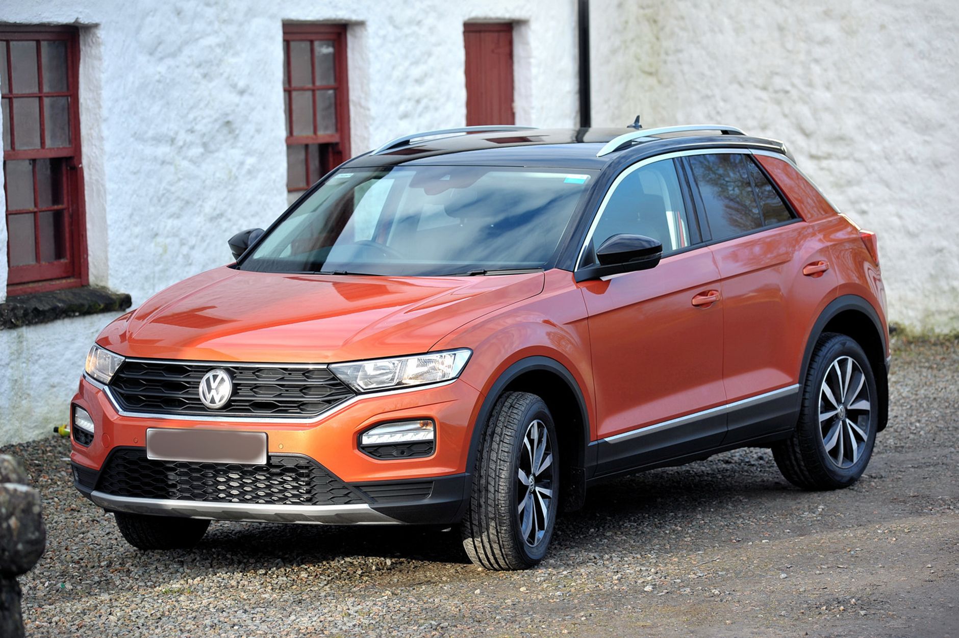 Pomarańczowy SUV Volkswagena na żwirze przy białym wiejskim budynku